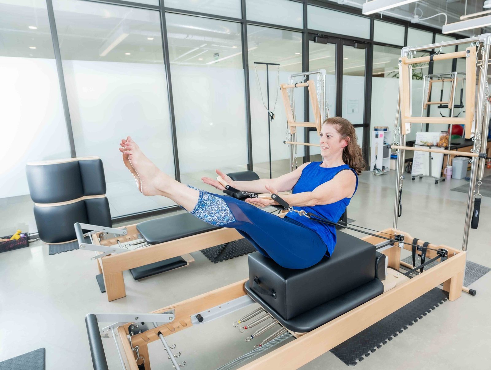 On the reformer in the Denver Pilates Girl studio, with the tower system and Denver light behind